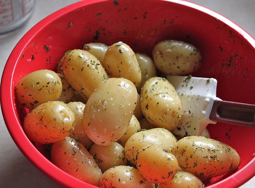 Stirring steamed potatoes with melted butter, salt, and herbs.