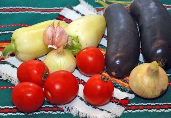 Свежие овощи для лечо из баклажанов на столе с вышитой скатертью и салфеткой