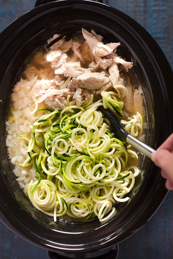 Adding the spiralized zucchini noodles to the slow cooker to allow them to cook, showing how the chicken has now been fully cooked and the vegetables are tender.