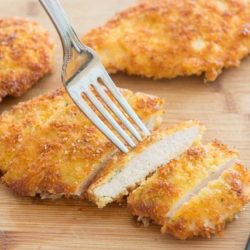 Parmesan Crusted Chicken Sliced On a Wooden Board with Fork Digging In