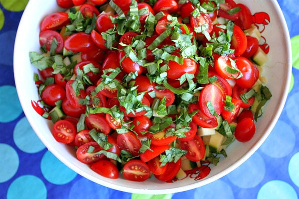 fresh basil added to a bowl of tomatoes set on a blue and green polka dot tablecloth