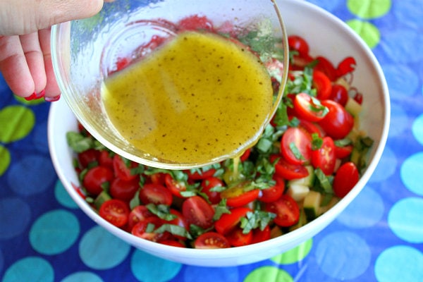 hand pouring dressing into bowl of fresh corn, zucchini and tomato salad, set on a blue and green polka dot tablecloth